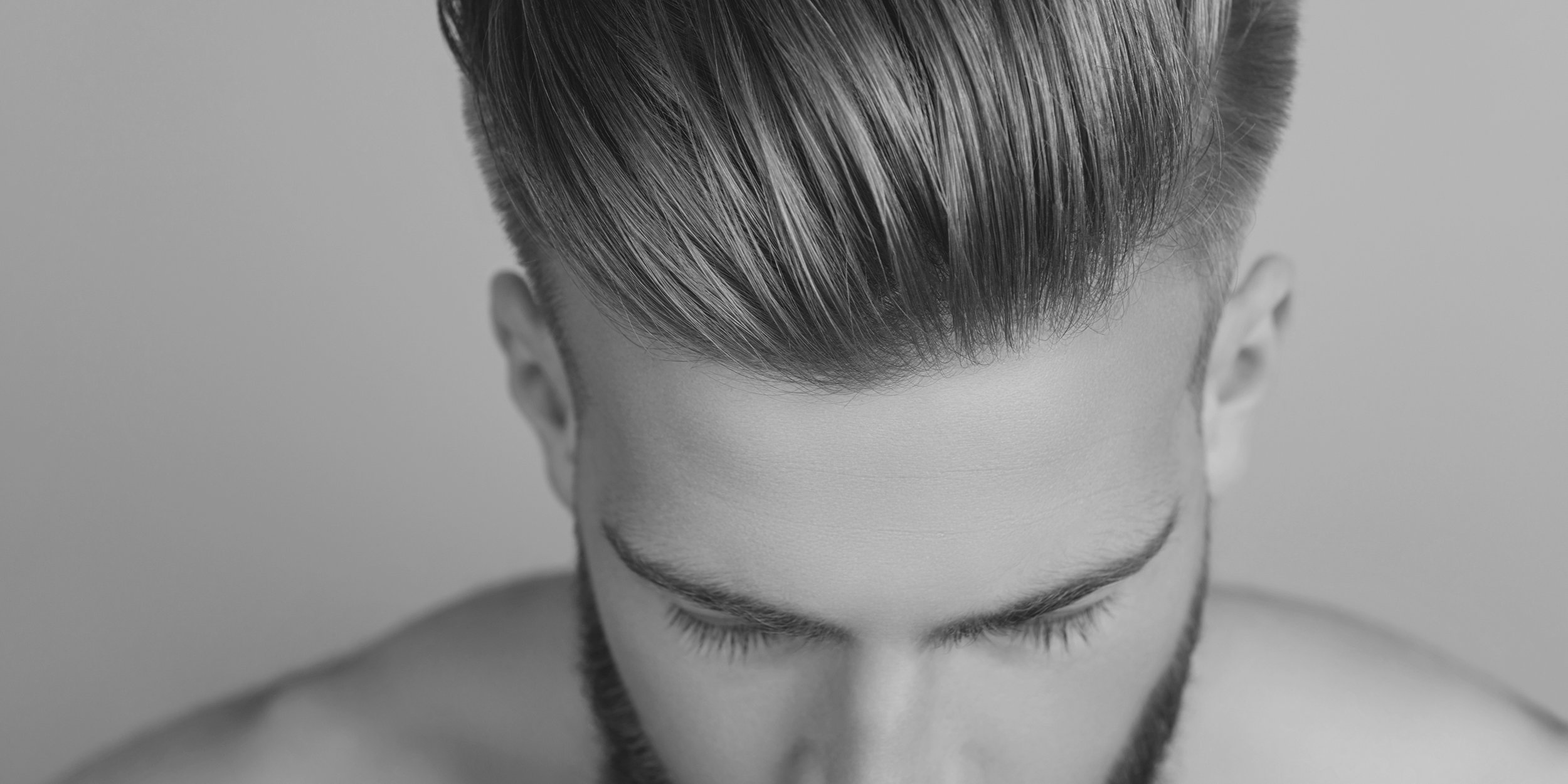 Black and white close-up of a person's head from above, showing their styled hair and closed eyes.
