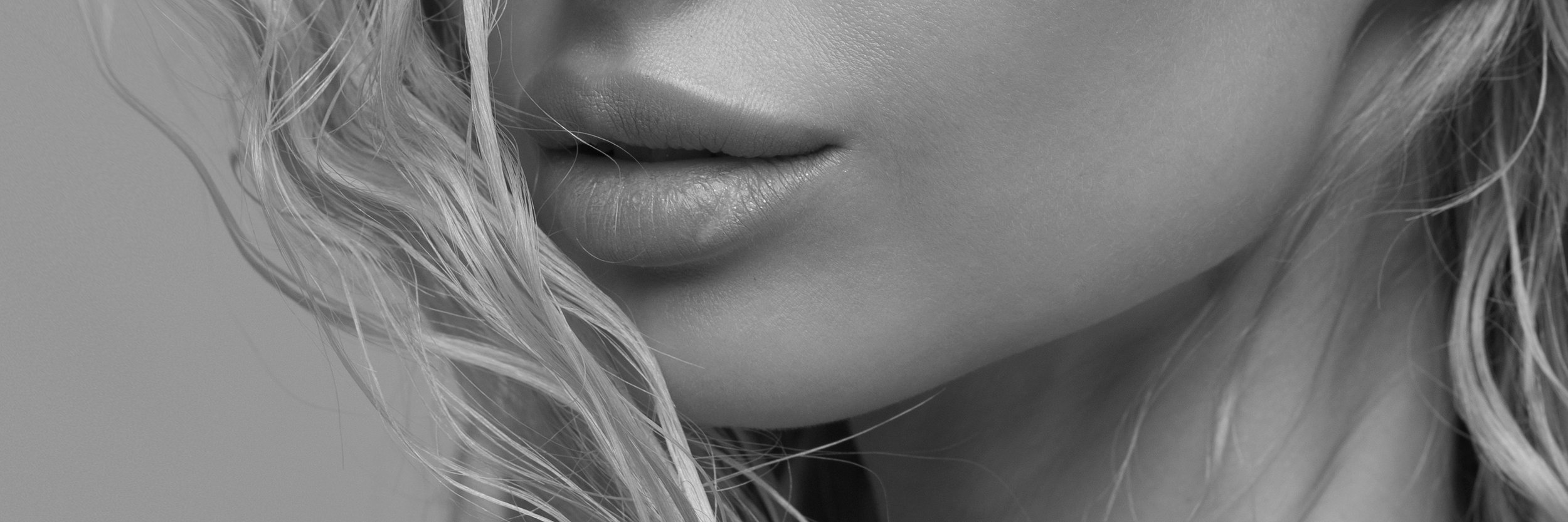 Close-up black and white image of a woman's lips and chin with wavy blonde hair.