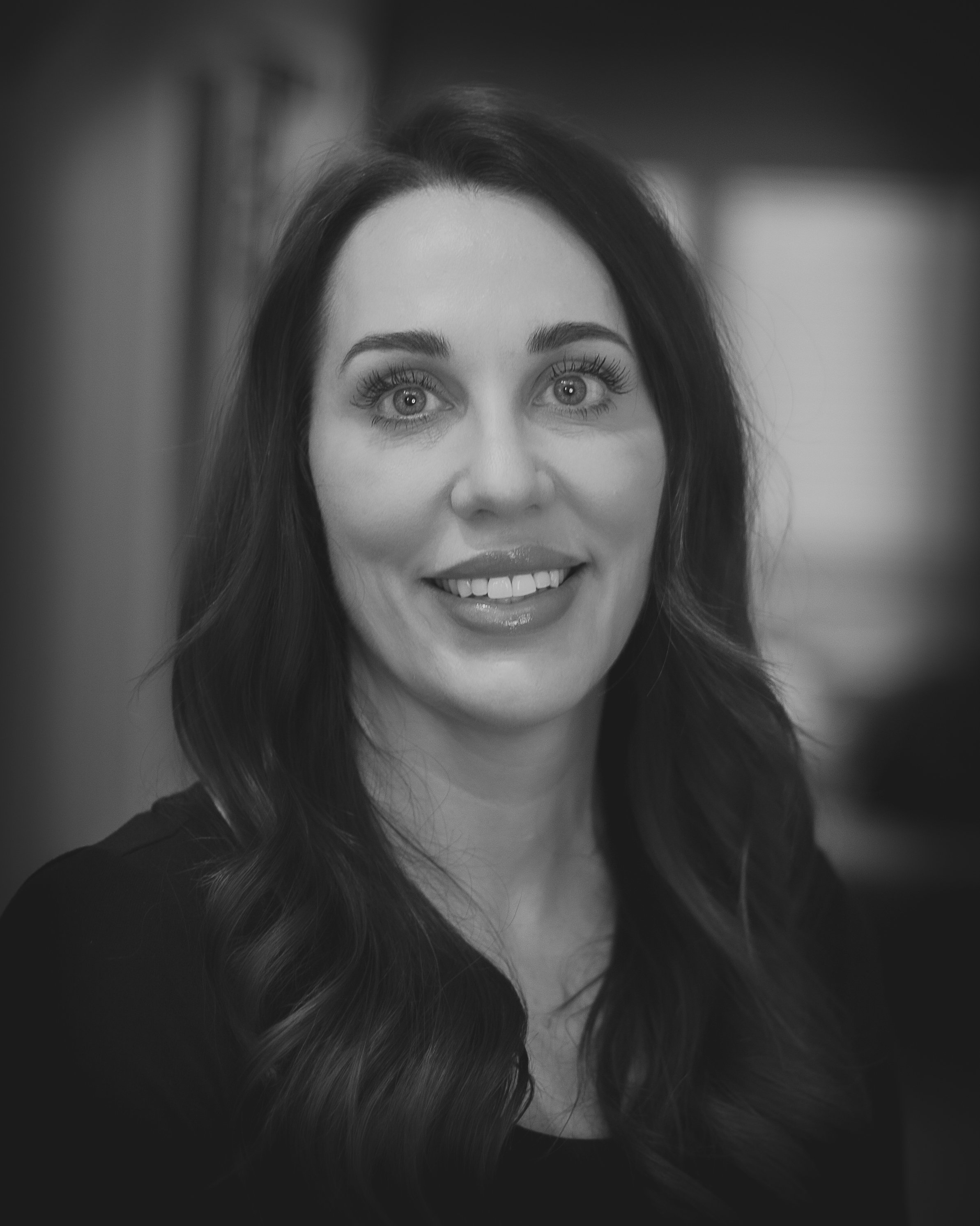 Black and white portrait of a woman with long wavy hair, smiling, in a professional setting.