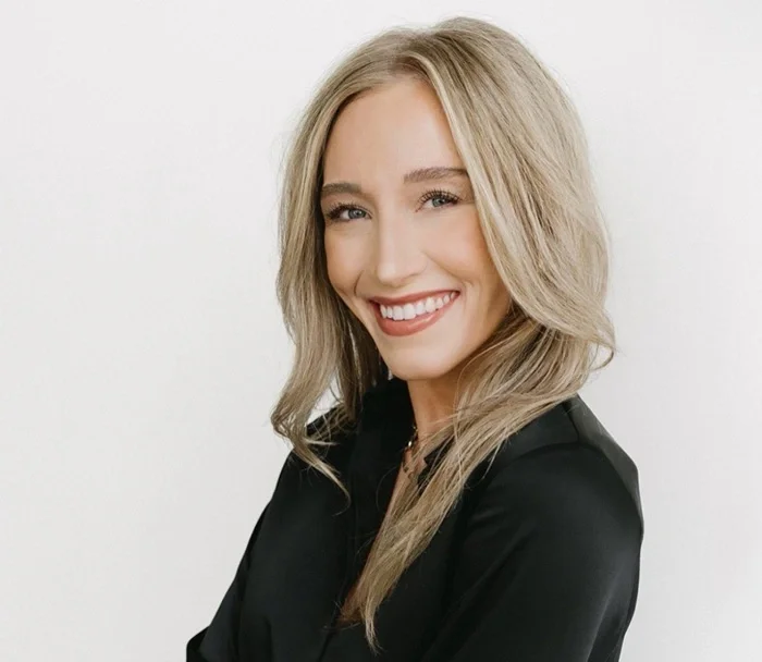 A smiling woman with blonde hair wearing a black top against a white background.
