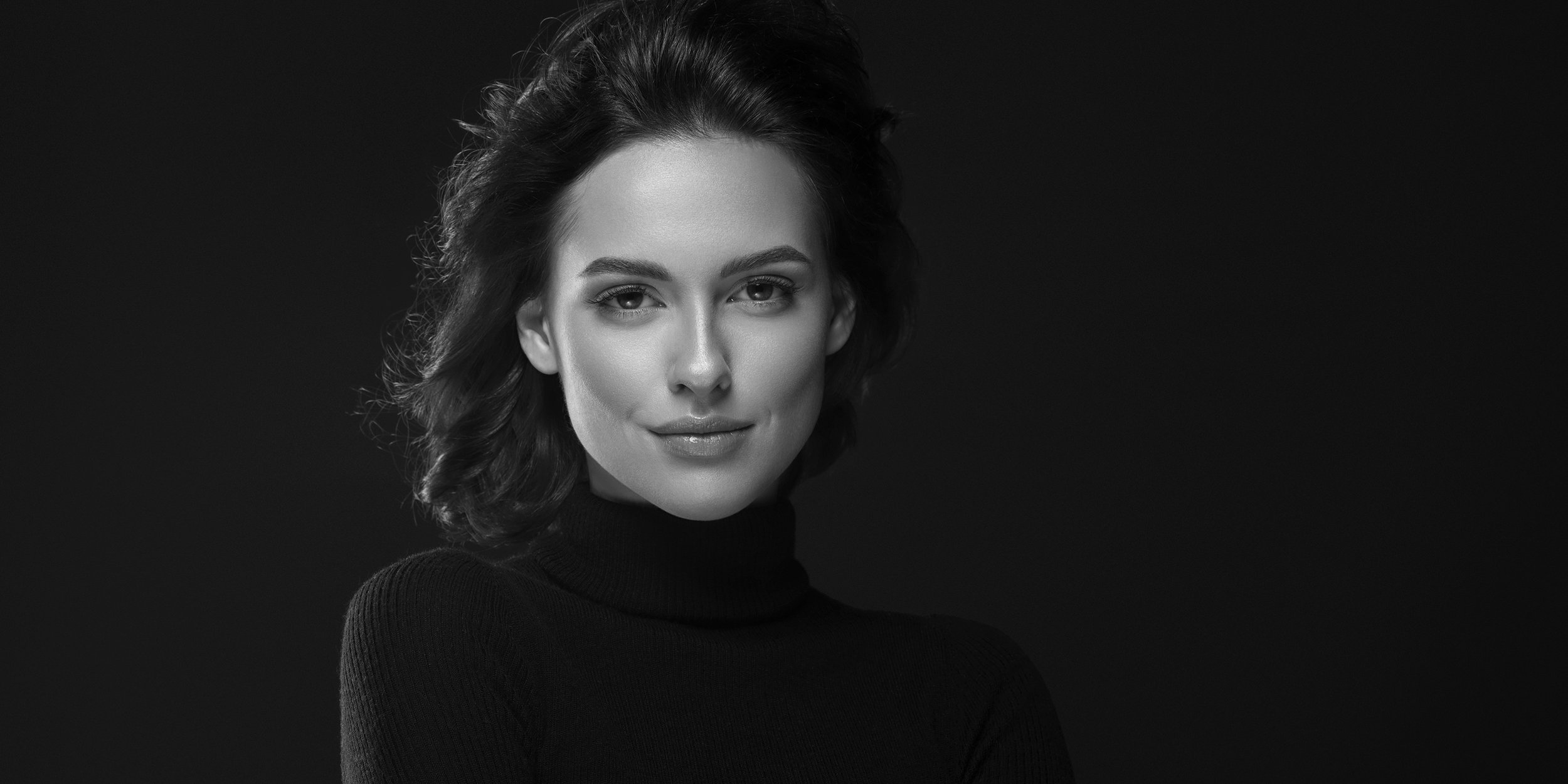 Black and white portrait of a woman in a turtleneck sweater against a dark background.