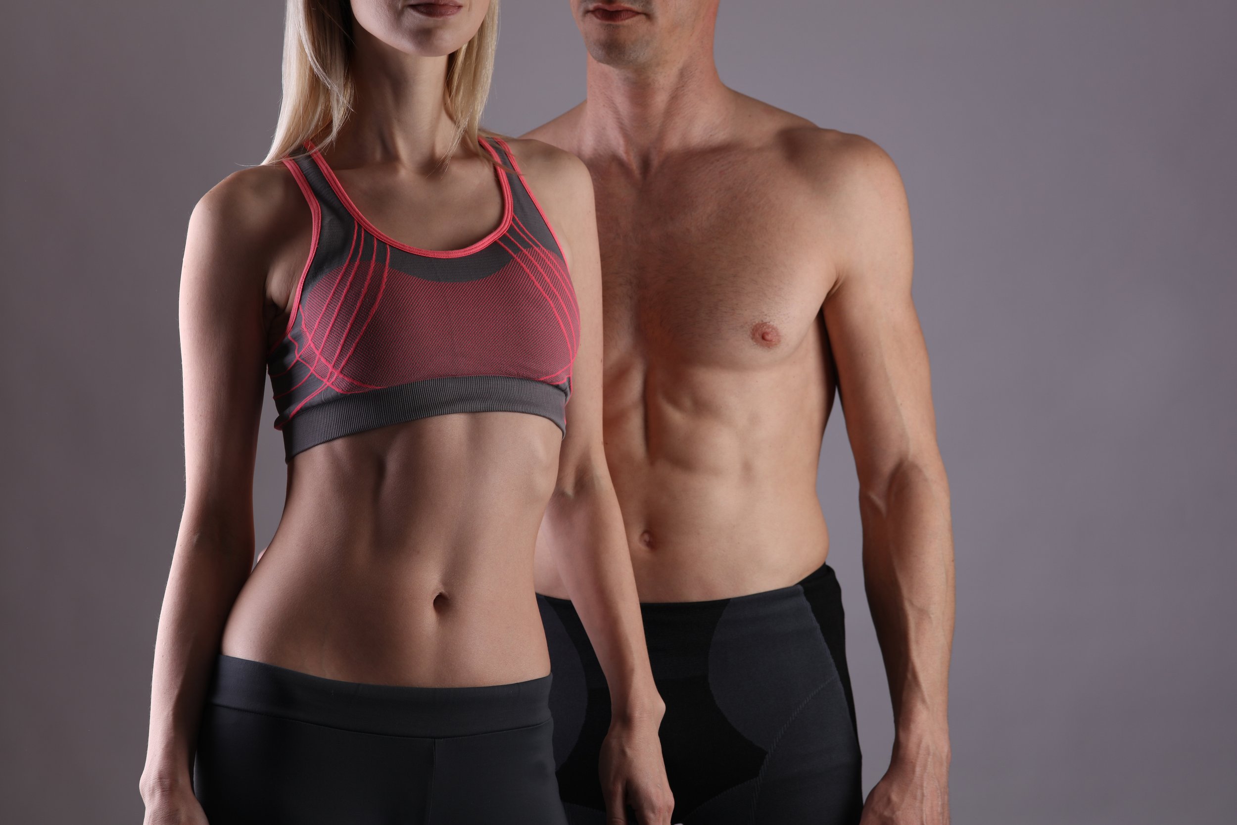 A woman and a man in athletic wear standing against a plain background.