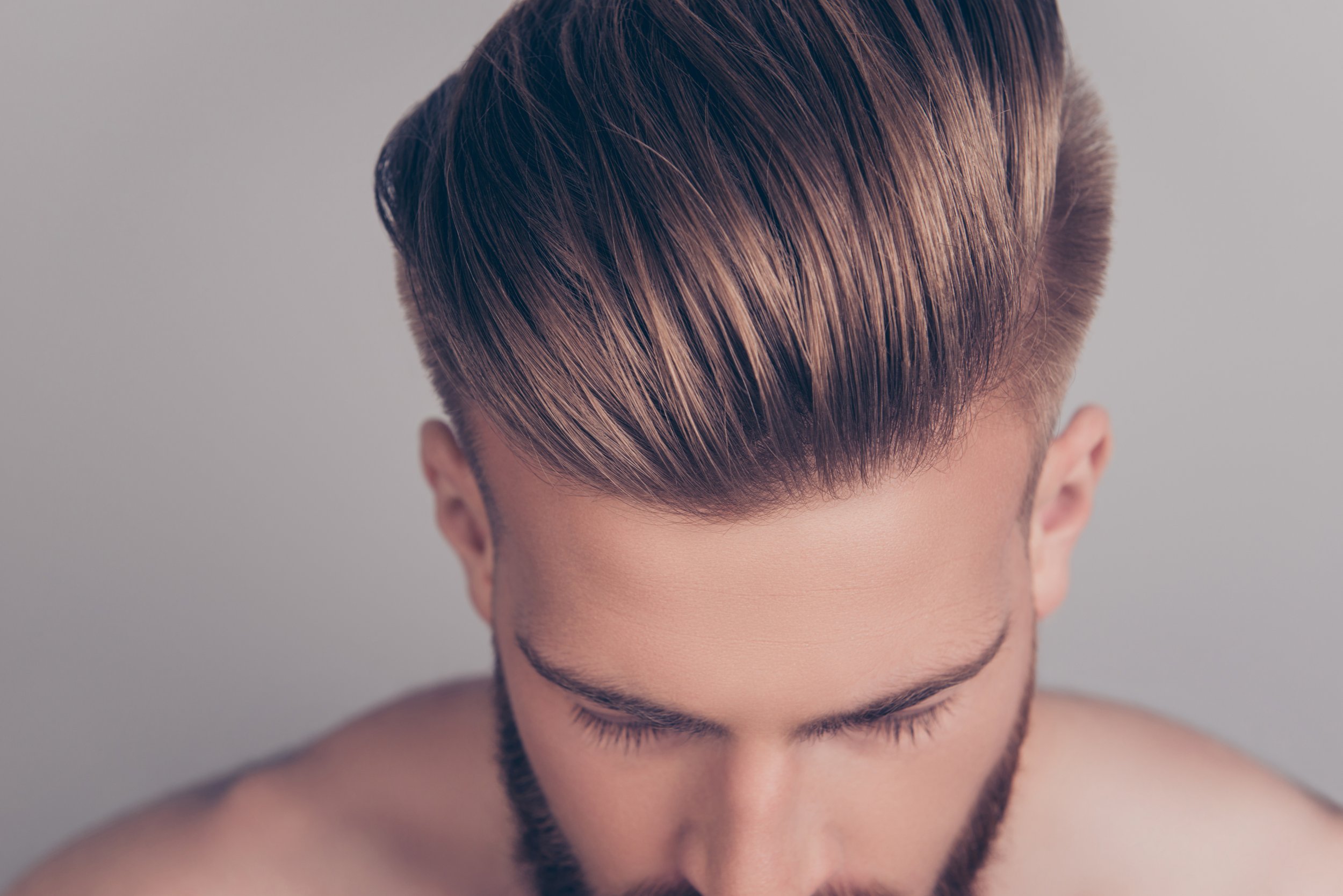 Close-up of a man's hairstyle with voluminous, neatly styled hair and a beard, looking downward.