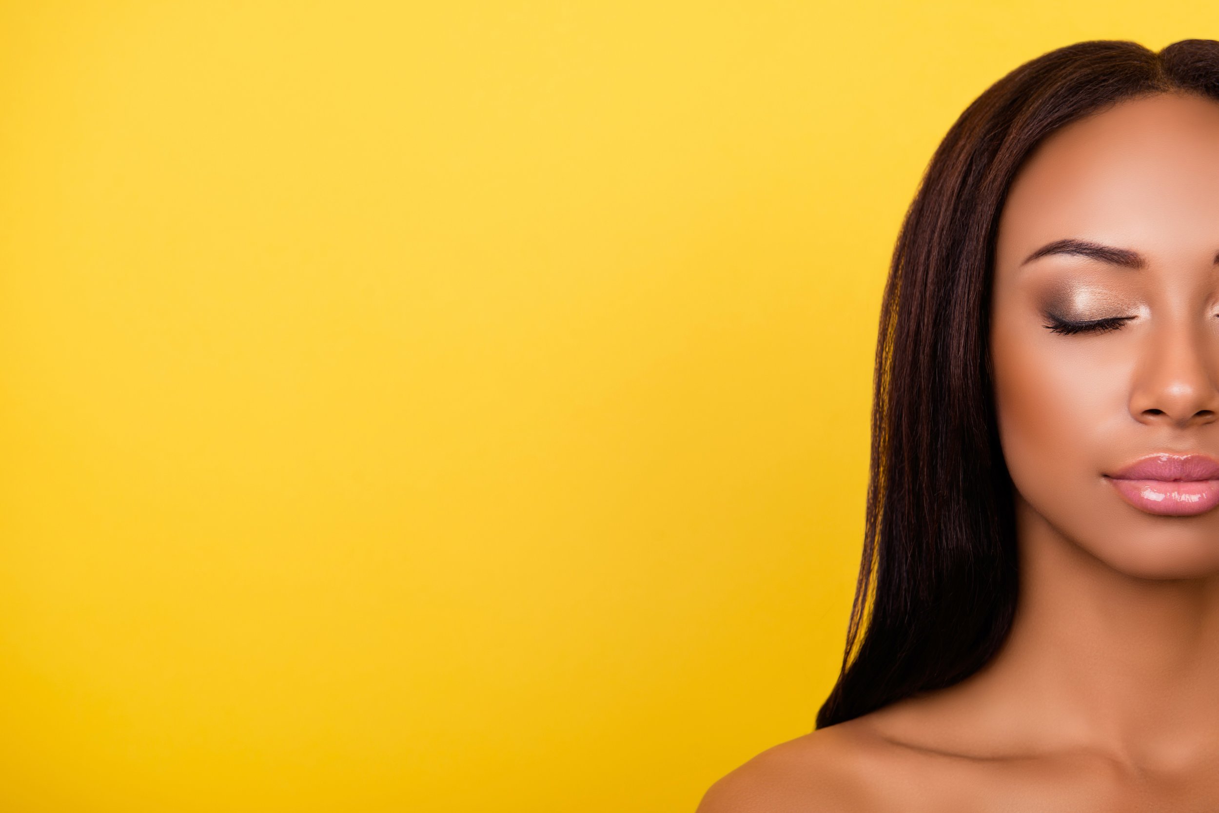 Close-up of a woman with closed eyes and long dark hair against a yellow background.