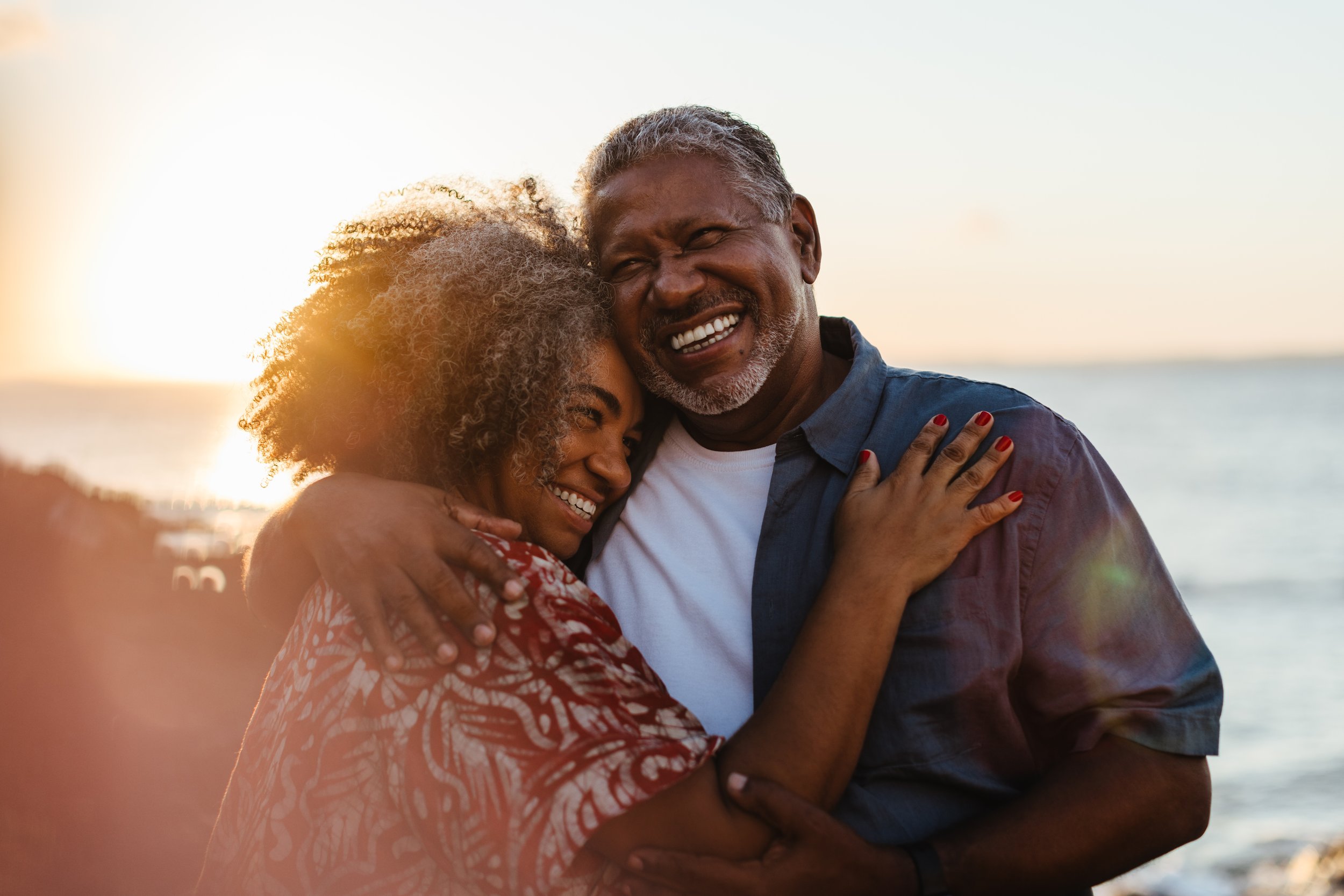 A happy couple hugs on the beach during sunset, embracing and smiling.